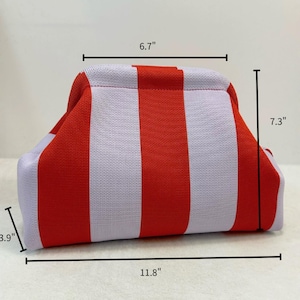 May include: A knit pouch featuring vertical red and light purple stripes. The pouch has a structured frame opening and dimensions of 6.7 inches in width at the top, 11.8 inches in width at the base, 7.3 inches in height, and 3.9 inches in depth.
