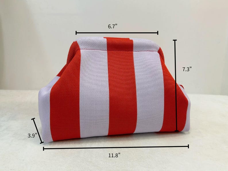 May include: A knit pouch featuring vertical red and light purple stripes. The pouch has a structured frame opening and dimensions of 6.7 inches in width at the top, 11.8 inches in width at the base, 7.3 inches in height, and 3.9 inches in depth.
