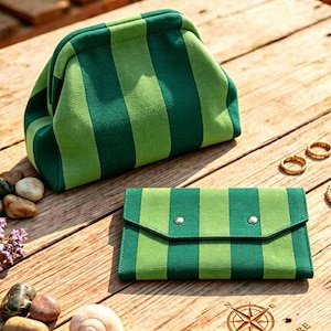 May include: A structured pouch with a kiss-lock closure and a matching rectangular wallet, both featuring a vertical striped pattern in alternating shades of dark forest green and light lime green, crafted from a textured fabric material.