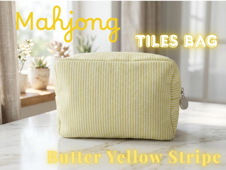 May include: A butter yellow striped Mahjong Tiles Bag with a zipper closure. The bag is rectangular and has a vertical stripe pattern. The text "Mahjong TILES BAG Butter Yellow Stripe" is displayed in yellow.