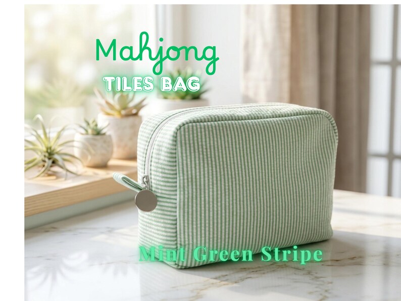 May include: A mint green striped Mahjong Tiles Bag with a zipper closure and a silver-tone charm. The bag is rectangular and sits on a marble surface. Text on the bag reads "Mahjong Tiles Bag" and "Mint Green Stripe."