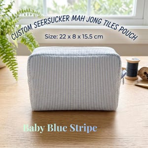 May include: A baby blue and white striped seersucker pouch for Mah Jong tiles. The pouch measures 22 cm long, 8 cm wide, and 15.5 cm high. The text on the pouch reads "CUSTOM SEERSUCKER MAH JONG TILES POUCH" and "Baby Blue Stripe".