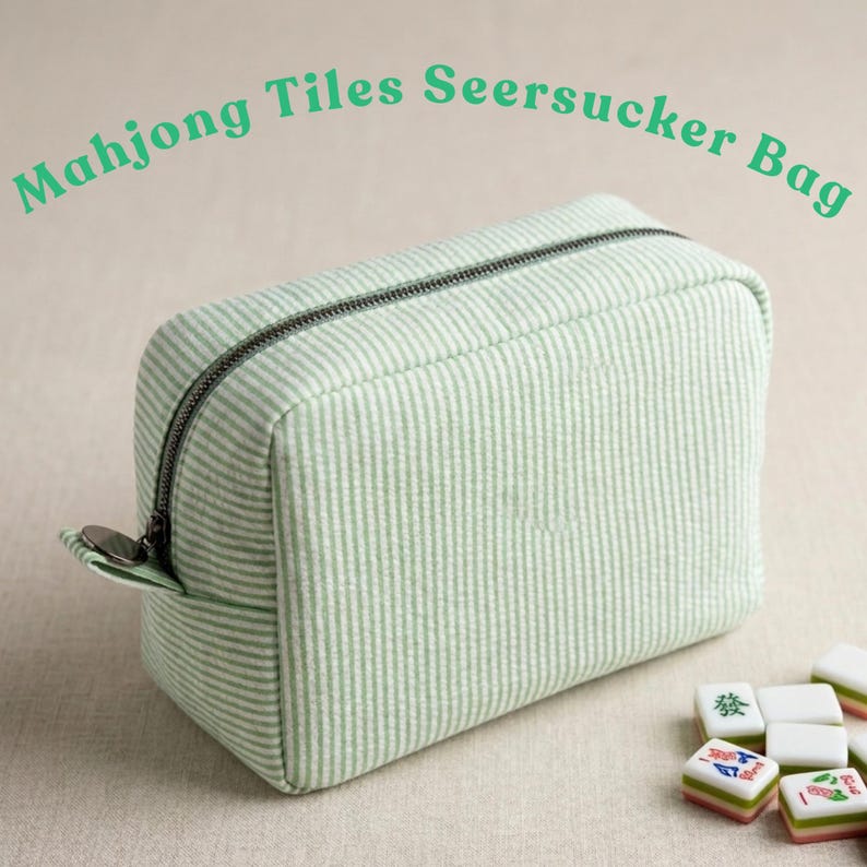May include: A rectangular, light green and white striped seersucker bag with a black zipper and a small metal pull tab. The text "Mahjong Tiles Seersucker Bag" is above the bag. Several Mahjong tiles are in the foreground.