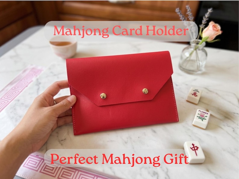 May include: A vibrant red Mahjong card holder with gold button fastenings. The image includes the text "Mahjong Card Holder" and "Perfect Mahjong Gift". Several Mahjong tiles are also visible.