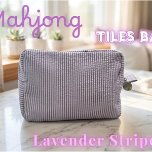 May include: A lavender and white striped Mahjong Tiles Bag. The rectangular bag has a zipper closure with a metal charm and a small fabric loop. The text "Mahjong Tiles Bag" and "Lavender Stripe" are displayed on the image.
