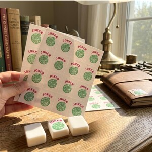 May include: Sheets of stickers and three tiles for a Mahjong game. The stickers have a green circular design with the word "JOKER" in red. The tiles are white with a green design.