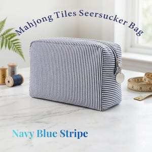 May include: A navy blue and white striped seersucker bag with the text "Mahjong Tiles Seersucker Bag" and "Navy Blue Stripe". The bag has a zipper closure and a silver charm. The bag is rectangular and appears to be made of fabric.