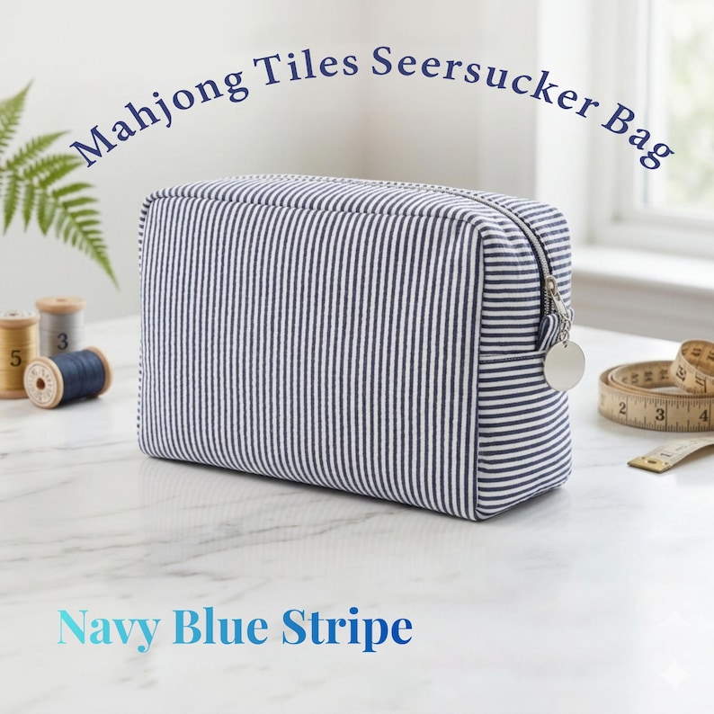 May include: A navy blue and white striped seersucker bag with the text "Mahjong Tiles Seersucker Bag" and "Navy Blue Stripe". The bag has a zipper closure and a silver charm. The bag is rectangular and appears to be made of fabric.