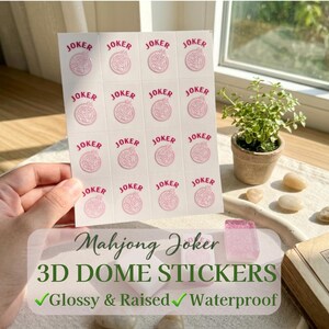 May include: Sheet of white Mahjong Joker 3D dome stickers with pink text and graphics. The stickers are glossy, raised, and waterproof. The sheet is held by a hand near a window with a small potted plant.