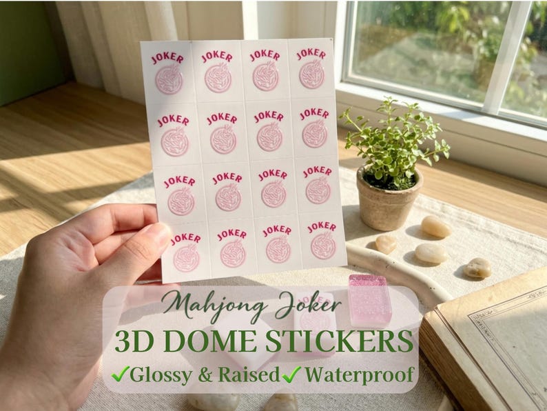 May include: Sheet of white Mahjong Joker 3D dome stickers with pink text and graphics. The stickers are glossy, raised, and waterproof. The sheet is held by a hand near a window with a small potted plant.