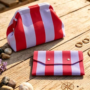 May include: A red and light purple striped frame pouch and a matching rectangular envelope-style wallet with two silver-toned snap closures. The items feature a bold vertical stripe pattern in a vibrant red and a soft, muted light purple color.
