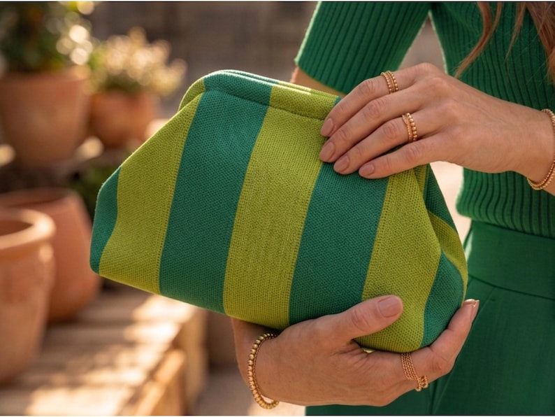 Pode incluir: Uma bolsa clutch estruturada com um padr&atilde;o de riscas verticais arrojado em tons alternados de verde floresta e verde lima. A bolsa tem uma textura macia semelhante a malha e um fecho superior curvo em estilo de moldura.