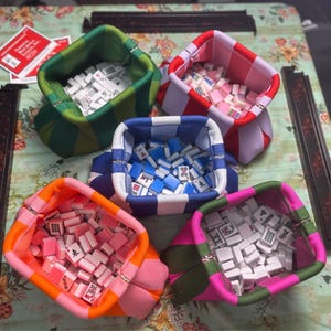 May include: Five fabric pouches with striped patterns in green, red, blue, orange, and pink, each filled with small white, blue, or pink mahjong tiles. The pouches feature a structured, open-top design with a metal frame closure at the top edge.