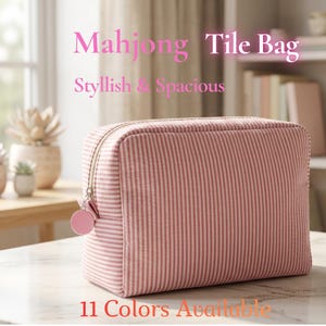 May include: A pink and white striped Mahjong Tile Bag with a zip closure and a pink charm. The bag is rectangular and sits on a marble surface. Text on the image reads "Mahjong Tile Bag, Stylish & Spacious, 11 Colors Available."