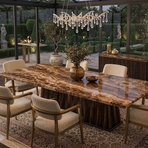May include: A rectangular dining table with a polished brown wood grain surface and a dark vertical slatted base, surrounded by six cream-coloured upholstered chairs with gold metal frames, positioned under a crystal chandelier.
