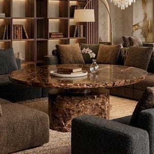 Könnte beinhalten: Ein luxuriöses Wohnzimmer mit einem großen, ovalen Couchtisch mit brauner Marmorplatte und zylindrischem Sockel. Der Raum umfasst ein weiches Sofa, Sessel, ein Bücherregal und eine Stehlampe, die eine warme und einladende Atmosphäre schaffen.
