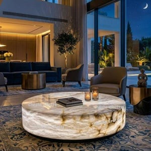 Könnte beinhalten: Ein modernes Wohnzimmer mit einem großen, runden, beleuchteten Couchtisch. Der Tisch hat eine marmorähnliche Optik und ist von Sitzgelegenheiten umgeben, darunter ein Sofa und Sessel. Große Fenster bieten einen Blick auf eine Nachtszene.