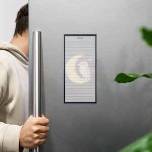 May include: A rectangular magnetic notepad with a dark blue border is displayed on a refrigerator. The notepad features a crescent moon and owl design with the word "Notes" at the top. The notepad has lined paper.