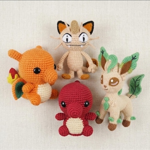 May include: Four handmade crochet plush toys featuring a bright orange dragon with a flame tail, a tan bipedal cat-like creature, a small round red creature with a cream belly, and a cream-colored quadruped with green leaf-like ears and tail.