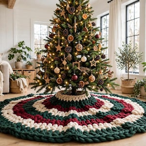 May include: A round, chunky knit Christmas tree skirt featuring concentric rings of dark green, deep red, and cream-colored yarn. The thick, textured fabric is crafted with large stitches and is positioned at the base of a decorated tree.