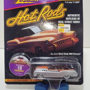 May include: Johnny Lightning Hot Rods die-cast car, silver and orange with black accents. The packaging includes the text "Hot Rods" and "Limited Edition." Collector No. 10, Bumongous by Troy Trepanier.