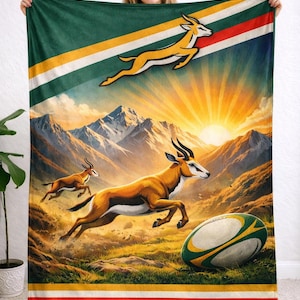 May include: A green, white, and gold blanket featuring a rugby ball and leaping gazelles against a backdrop of mountains and a sunset. The blanket has stripes of red, white, and gold.