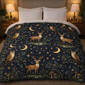 Puede incluir: Una funda nórdica azul oscuro con un diseño de noche de bosque. El diseño incluye ciervos, búhos, lunas crecientes, estrellas y elementos florales. La ropa de cama tiene un borde blanco y está sobre una cama con almohadas blancas.