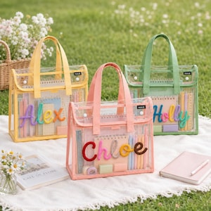 May include: Three transparent tote bags with colored trim and handles in yellow, pink, and green. Each bag features a name in fuzzy, multi-colored letters on the front: Alex, Chloe, and Holly. Inside each bag are notebooks, pens, and rulers.