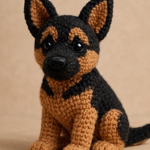 Pode incluir: Um filhote de pastor alemão de crochê feito à mão em preto e castanho. O cão amigurumi tem orelhas grandes e eretas, um nariz preto e uma cauda pequena. O filhote está sentado, com as patas dianteiras.