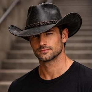 May include: A black cowboy hat with a braided band. The hat has a wide brim and a slightly distressed appearance. The hat is worn by a person wearing a black shirt.