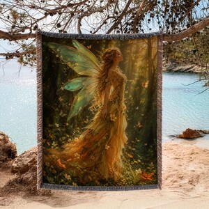 May include: A rectangular woven throw blanket featuring a detailed illustration of a fairy with large translucent green wings and a flowing yellow gown standing in a sunlit forest filled with small flowers and butterflies, with fringed edges.