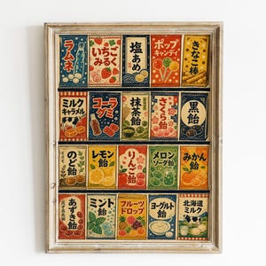 May include: A framed rectangular print featuring a grid of twenty vintage-style Japanese candy packaging designs. Each individual rectangular label displays colorful illustrations of various sweets, fruits, and beverages with Japanese text characters.