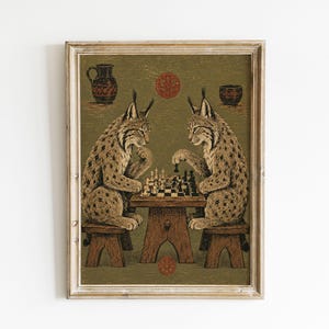 May include: A framed wall art print featuring two lynxes sitting on wooden stools, facing each other while playing a game of chess on a wooden table. The background is a muted olive green with two small red circular motifs, a pitcher, and a bowl.