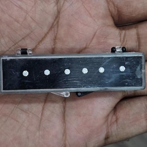 May include: A black rectangular object with five evenly spaced, circular, white embellishments. The object has a silver frame and clear plastic hinges. The item is held in a hand.