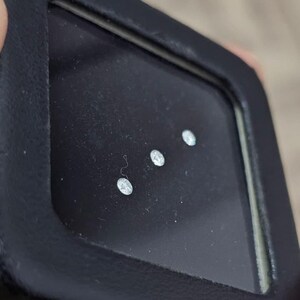 May include: A white ceramic mug with a black handle and the text "But First, Coffee" in a black, handwritten-style font. The mug is on a white surface.