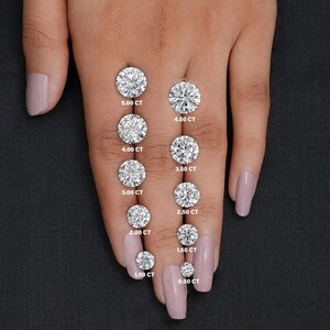 May include: A hand displays a series of round-cut diamonds, ranging from 0.50 CT to 5.00 CT. Each diamond is labeled with its carat weight in white text. The diamonds are set against a neutral background.