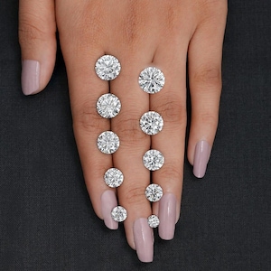 May include: A collection of round-cut diamonds of varying sizes, displayed on a hand with polished nails. The diamonds sparkle, reflecting light, and are set against a dark background. The image showcases the brilliance and clarity of the gemstones.
