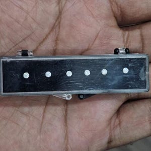 May include: A black rectangular object with five evenly spaced, circular, white dots. The object has a silver frame and small black hinges on each end. The object is held in a hand.