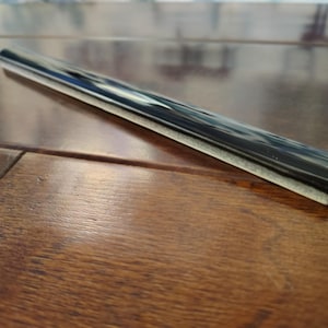 May include: A black and white rolling pin with a rectangular shape. The rolling pin is made of a dark material with a light-colored edge. The rolling pin is lying on a wooden surface.