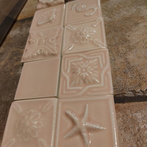 Puede incluir: Colección de baldosas de cerámica rosa con varios diseños en relieve, incluyendo flores y una estrella de mar. Las baldosas cuadradas tienen un acabado brillante, adecuadas para proyectos de decoración del hogar. Cada baldosa mide aproximadamente 10 cm x 10 cm.