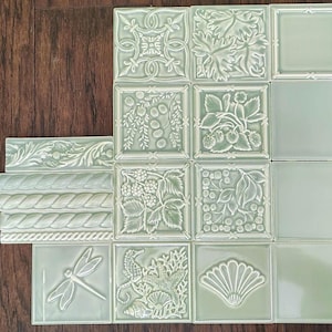 May include: A collection of light green ceramic tiles featuring various embossed designs including botanical patterns, a dragonfly, a seahorse, a starfish, and seashells, alongside several rectangular border tiles with rope and leaf motifs.