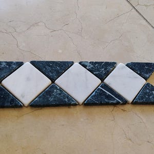 May include: A decorative tile border strip featuring a repeating geometric pattern of alternating white marble squares and dark green marble triangles arranged in a horizontal row with smooth, polished surfaces.