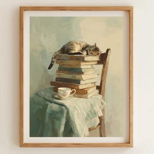May include: A framed print depicting a tabby cat asleep on a pile of books on a wooden chair. A teacup and saucer rest on a draped cloth. The artwork has a soft, painterly style with muted colours.