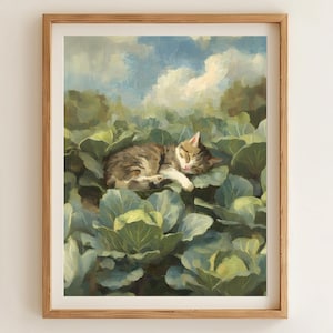 May include: A framed art print depicts a tabby cat sleeping peacefully amidst a bed of green cabbage leaves. The background features a blue sky with fluffy white clouds and hints of green trees, creating a serene, pastoral scene.