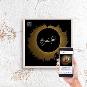 May include: A framed print featuring a gold sound wave design on a black background, with the name "Baxter" in script. A smartphone shows a dog image and text. The artwork is displayed on a white wall.