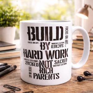 Könnte beinhalten: Weiße Keramiktasse mit schwarzem Text, der lautet: „BUILD BY HARD WORK NOT RICH PARENTS“. Die Tasse enthält auch die Sätze „Focus on Art“, „Zucked Clothing“ und „Sacred Clothing“. Die Tasse steht auf einer Holzoberfläche.