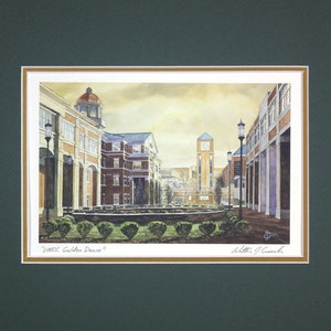 May include: Watercolor painting of a university campus scene, featuring buildings with red brick and white accents. The artwork includes a clock tower and a row of trimmed bushes. The title "UNCC Golden Dawn" is visible.