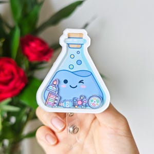 May include: A triangular shaker badge reel featuring a light blue liquid-filled flask with a winking face. Inside the clear casing are small floating charms including a Bunsen burner, test tubes, a water bottle, a molecule, and a petri dish.