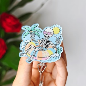 Peut inclure: Un enrouleur de badge représentant un squelette blanc portant des lunettes de soleil roses en forme de cœur, se relaxant dans une bouée rayée colorée. Le squelette tient une boisson avec un petit parasol, entouré d'un palmier, de vagues bleues et d'un soleil jaune.