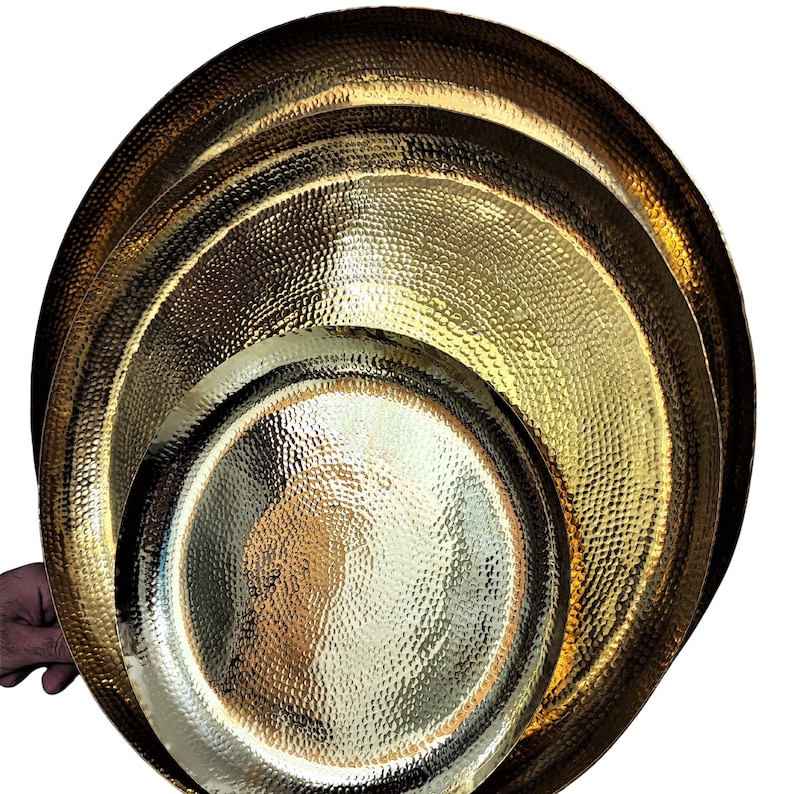 May include: A set of three hammered gold-colored metal serving trays. The trays are round with a textured surface and varying sizes. The largest tray is approximately 18 inches in diameter, the medium tray is 14 inches, and the smallest is 10 inches.